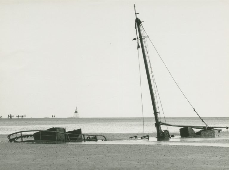 Een wrak ligt op het wad, half weggezonken in het zand.